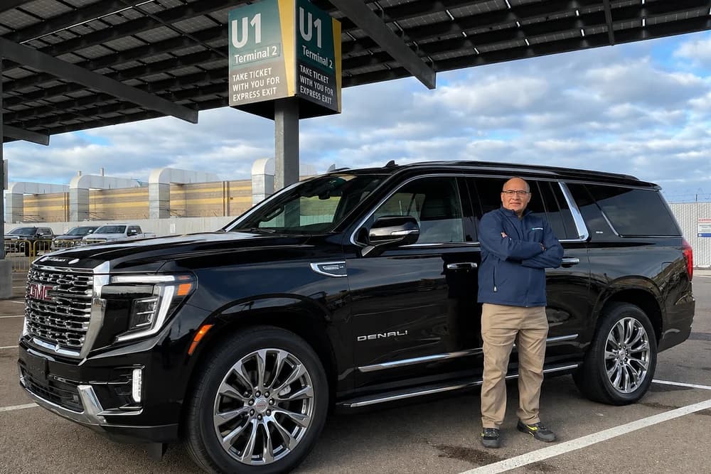 Driver standing beside a black private SUV at the airport